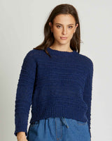 A model wearing a deep navy blue, textured 100% acrylic crew neck knit sweater with ribbed cuffs and hem.