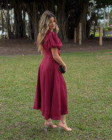 Woman wearing a burgundy pure linen midi dress with puff sleeves, standing in a park.