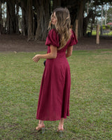 Woman wearing a burgundy pure linen midi dress with puff sleeves, standing in a park.