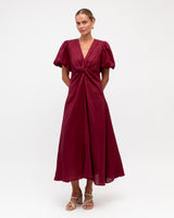 Burgundy pure linen event dress with puff sleeves, a V-neckline, and a knotted waist detail on a model.