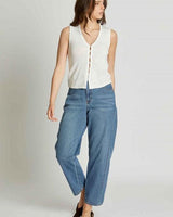 Woman wearing a white, sleeveless, button-down knit vest paired with relaxed-fit blue denim jeans.
