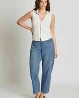 Model wearing a white, sleeveless, button-front knit vest paired with relaxed-fit blue denim jeans.