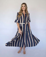 Woman wearing a navy, cream, and maroon striped midi shirt dress with a tie waist and short sleeves.