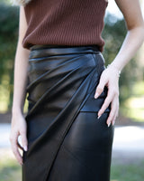 Black vegan leather Miley skirt featuring a flattering wrap-style design with elegant side ruching details.