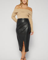 Black vegan leather midi skirt with a draped front, side pleats, and a front slit, paired with a beige off-shoulder top.