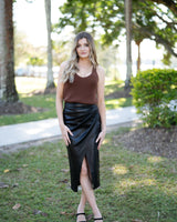 Model wearing a black vegan leather midi skirt with a flattering wrap-front design and side slit.