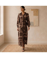 Model wearing a brown long-sleeve maxi dress with a geometric print, button-down front, and tie waist in a fluid fabric.