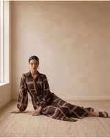 Model wearing a brown long-sleeve maxi dress with a geometric print, featuring a collared neckline and belted waist.