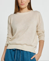 Model wearing a cream-colored relaxed fit sweater with a classic neckline and ribbed cuffs in soft knit fabric.