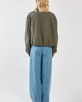 Back view of a woman wearing an olive green Murphy bomber jacket with an elasticated hem, paired with wide-leg blue jeans.