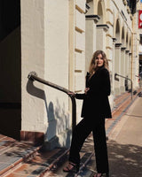 Woman wearing black velvet flared pants and a matching blazer, standing on outdoor stairs.