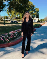 Woman wearing black stretch velvet flared pants with a matching blazer in an outdoor park setting.