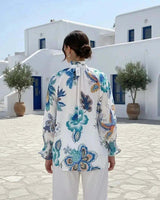 Woman wearing a white linen blend shirt with a blue and green botanical print, mandarin collar, and smocked 3/4 sleeves.