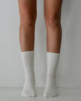 Milk-colored cable knit wool and cashmere blend socks worn on legs.