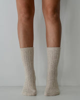 Natural cable-knit wool and cashmere blend socks with a textured ribbed design, worn on legs against a white background.