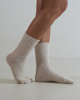 Beige cable knit wool and cashmere blend socks worn on feet, featuring a textured ribbed design.