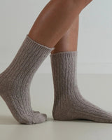 Beige cable-knit wool and cashmere blend socks with a ribbed cuff, worn on feet against a neutral background.