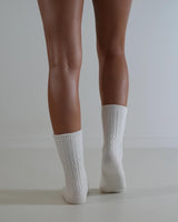 White cable knit wool and cashmere blend socks worn on legs, featuring a textured, classic design.