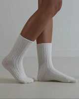 Cream-colored cable knit wool and cashmere blend socks worn on feet, featuring a textured ribbed design.