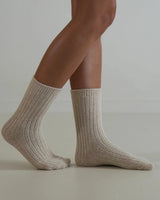 Beige ribbed wool and cashmere blend socks worn on feet, featuring a soft, textured knit design for winter comfort.