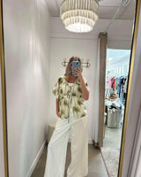 Sage green palm print short-sleeve shirt in Tencel-viscose blend with a front tie detail, worn with white wide-leg pants.
