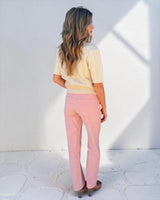 Woman wearing pink corduroy straight-leg jeans with back pockets and a cream cable-knit sweater.