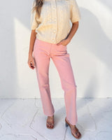 Woman wearing a light yellow top and pink pants against a white background