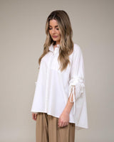 Woman wearing a white oversized cotton poplin shirt with unique pull-detail sleeves and a relaxed button-up fit.