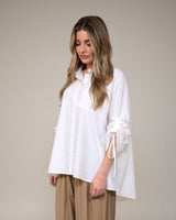 Woman wearing a white blouse and beige pants on a plain background