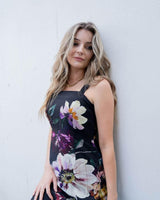 Blonde woman wearing a black cotton-nylon Providence dress with a bold floral print and square neckline.