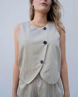 Beige wrap vest with thin vertical stripes, featuring a curved hem and three dark buttons on a soft fabric.