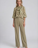 Model wearing a sheer olive plaid pussybow blouse with elasticated sleeves and tailored olive trousers.