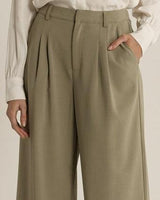 Sage green relaxed-fit trousers with front pleats, side pockets, and a tailored zip fly closure.