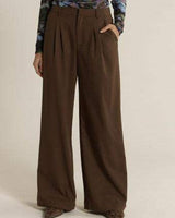 Chocolate brown relaxed-fit trousers featuring front pleats, side pockets, and a tailored zip fly closure.