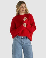 Woman wearing a soft, oversized red knit sweater with a ribbed neckline and dropped shoulders, paired with blue denim jeans.