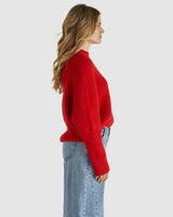 Woman wearing a red, oversized, fluffy knit sweater with a ribbed neckline and dropped shoulders paired with jeans.