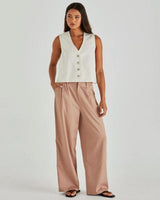 Off-white cotton denim vest with a V-neck, shank button front, and princess seams, styled with wide-leg trousers.