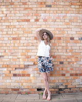 Woman wearing a white cotton denim vest with shank buttons and princess seams against a brick wall.