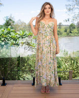 Woman wearing a lightweight, floor-length rayon sun dress with a green and pink tropical leaf print and spaghetti straps.