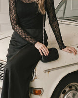 Woman wearing a black long-sleeve lace top and sleek pencil skirt, styled with a matching black clutch bag.
