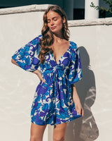 Blue and purple floral print V-neck playsuit with puff sleeves and adjustable bust tie, featuring a shirred back and pockets.