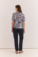 Anika Frill Neck Blouse in a blue and white abstract print with a gathered neckline, worn with dark denim jeans.