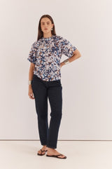 Anika Frill Neck Blouse in a blue abstract print with a gathered neckline and short sleeves, worn with dark denim jeans.