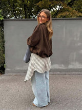 Woman wearing an oversized brown suede bomber jacket with dropped shoulders and an elasticated hem over a plaid shirt.
