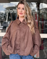 Woman wearing an oversized, earthy rose suede bomber jacket with a stand-up collar and zip-front closure.