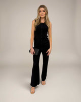 Woman wearing a black sleeveless ribbed knit vest and matching flared trousers with a small black clutch.