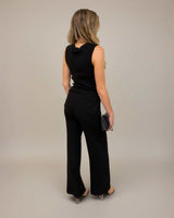 Woman wearing a black sleeveless knit vest with ribbed trims and matching wide-leg trousers from the back.