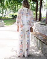 Woman wearing wide-leg Solara pants in a cream floral print with linen-blend fabric and contrast border hem.