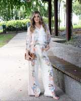 Woman wearing wide-leg Solara pants in a white floral print with a contrast border hem and elasticated waistband.