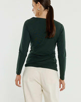Bottle green long-sleeve jersey top with a side knot detail and boat neckline, worn with cream trousers.